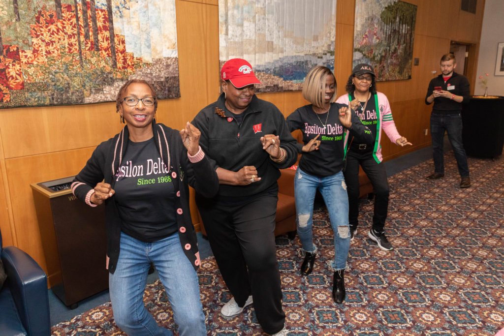 Four alumni members of the Alpha Kappa Alpha sorority perform a coordinated stroll routine around a room.