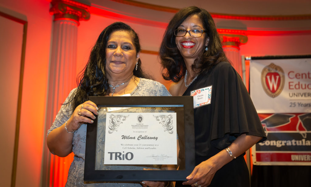 Two women hold a large award plaque while smiling facing camera.