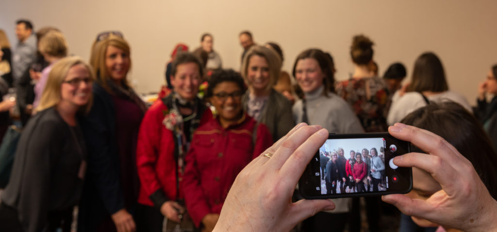 A phone screen with the camera active is in the foreground, with the subjects of the phone's camera blurred in the background.