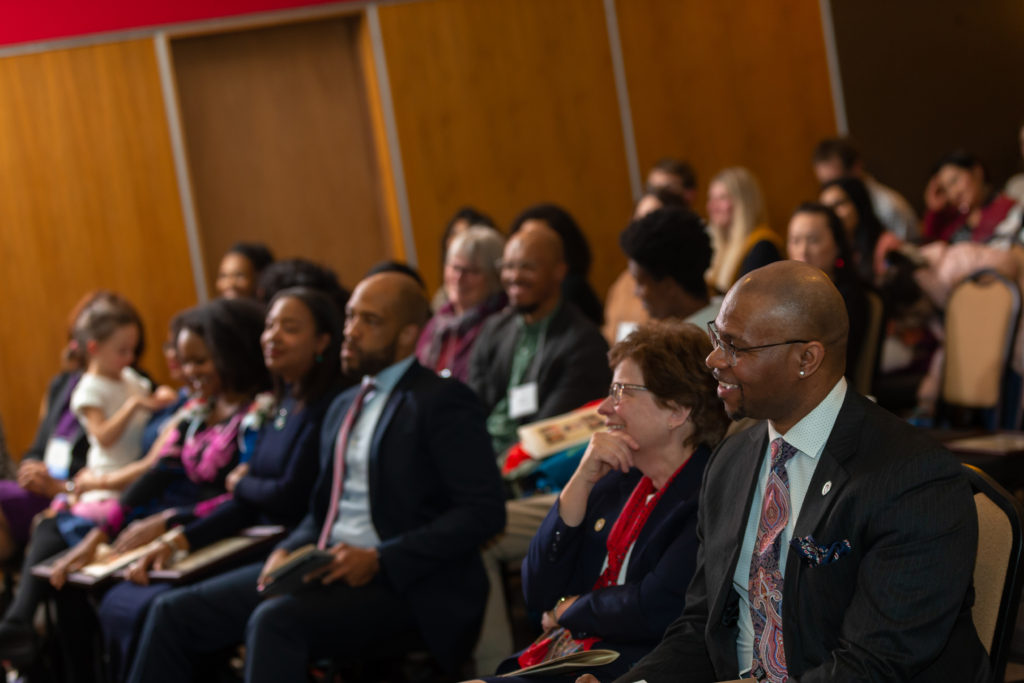People in the audience smile as they watch a speaker. In the audience are Lt. Gov. Mandela Barnes, Chancellor Becky Blank and Deputy Vice Chancellor Patrick J. Sims.