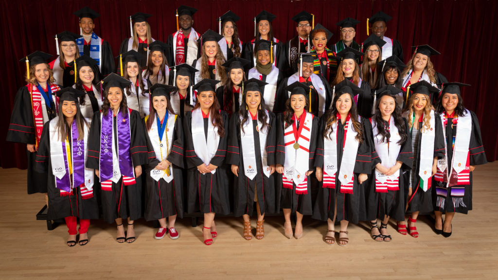 Thirty-three graduating seniors from the Center for Educational Opportunity pose in their graduation robes and caps with white stoles draped over their shoulders.