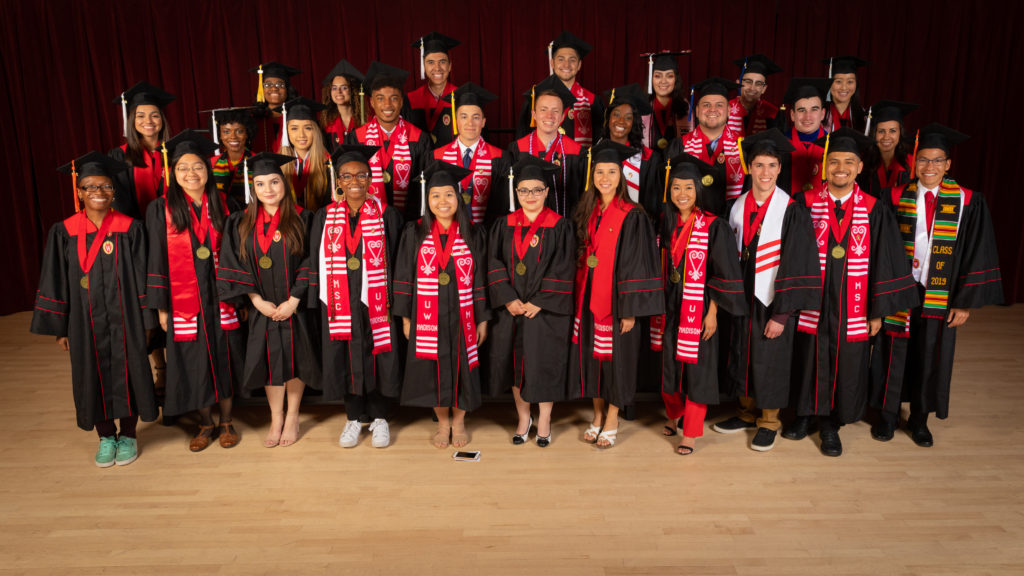Twenty-eight graduating seniors from the Chancellor's Scholarship Program pose in their graduation robes and caps with round, gold medallions hanging around their necks.