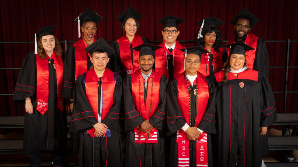Nine graduating seniors and one staff member from the First Wave program pose in their graduation robes and caps with red stoles draped over their shoulders.