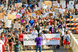 A large crowd of demonstrators wearing face masks and carrying signs in support of Black Lives Matter and social justice reform.