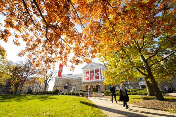 People walking among bright orange fall leaves on Bascom hill with Bascom Hall in the background.