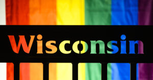 A rainbow pride flag hangs behind the word "Wisconsin" cut out of side of a bus shelter.