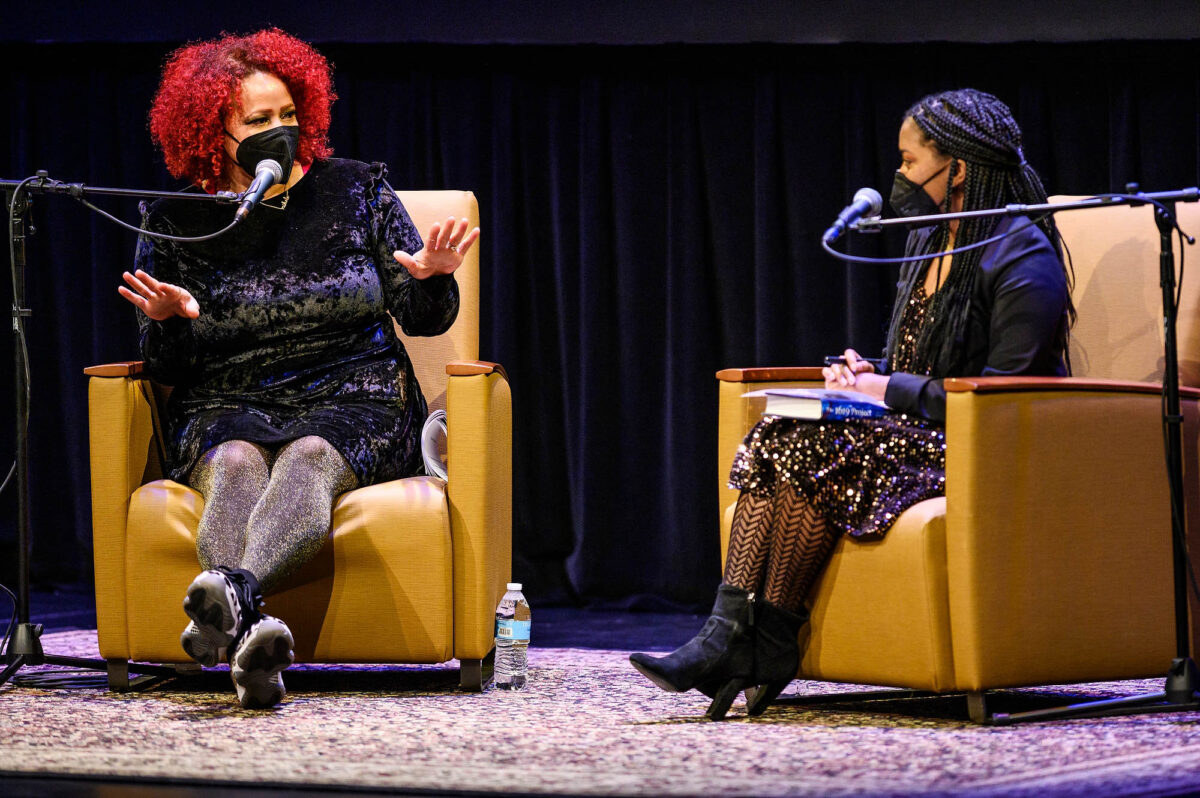 Nikole Hannah-Jones and student Tamia Fowlkes sit in yellow chairs on a rug on stage speaking into microphones.