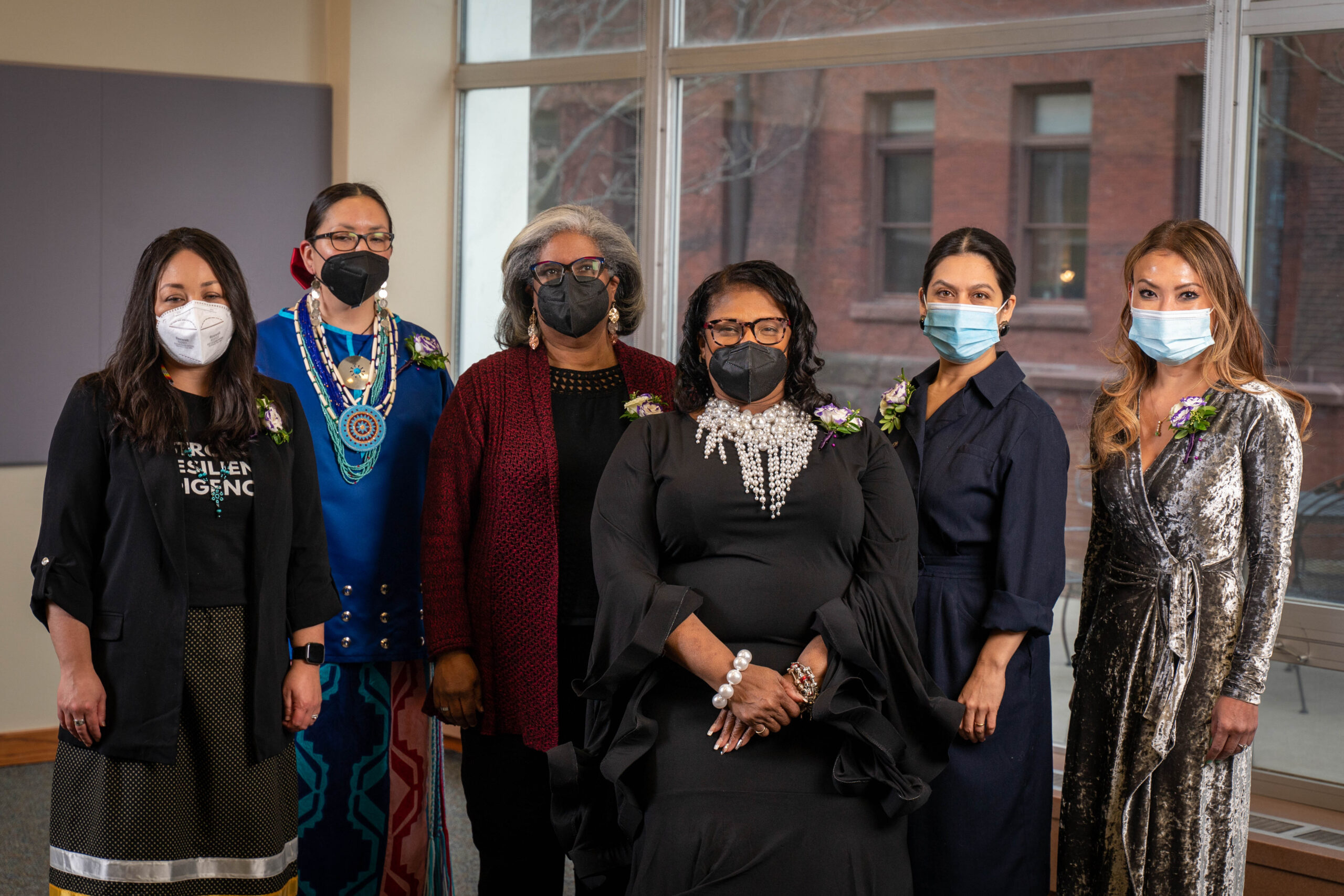 Six women of color in formal attire and face masks pose for a group photo.