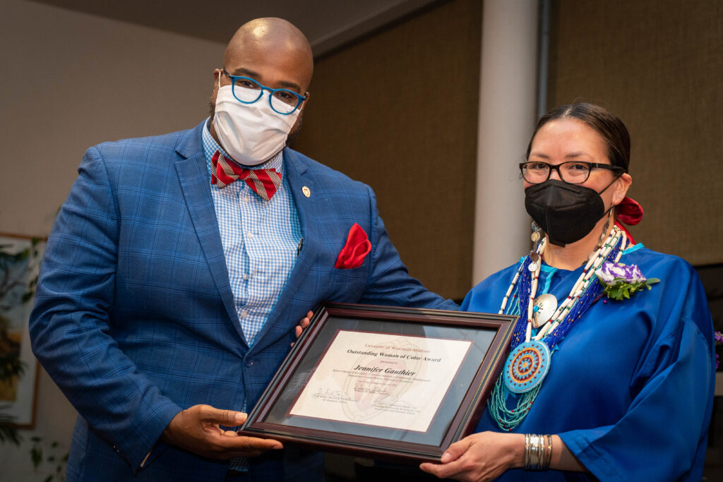 LaVar Charleston wearing a blue suit and red bow tie stands with Jennifer Gauthier in a blue Native American dress and beaded jewelry holding a plaque.