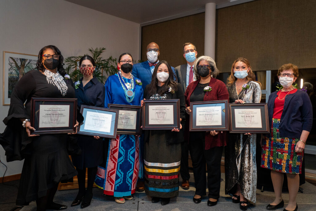 Nine people wearing formal attire and face masks stand on stage posing for a group photo.
