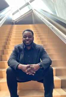 Montee Ball sits and smiles at the bottom of a flight of stairs wearing a dark suit.
