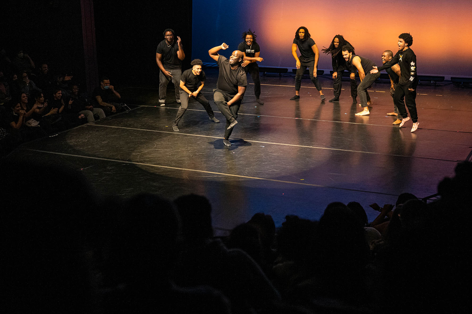 A group of performers dressed in black perform choreography on stage.