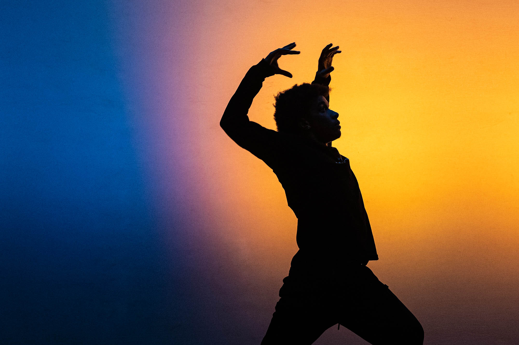 Silhouette of a person dancing with arms raised with blue and yellow lights behind them.