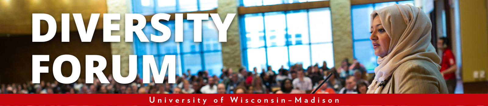 A woman wearing a head scarf speaks into a microphone in front of a large audience with the words "Diversity Forum. University of Wisconsin–Madison."