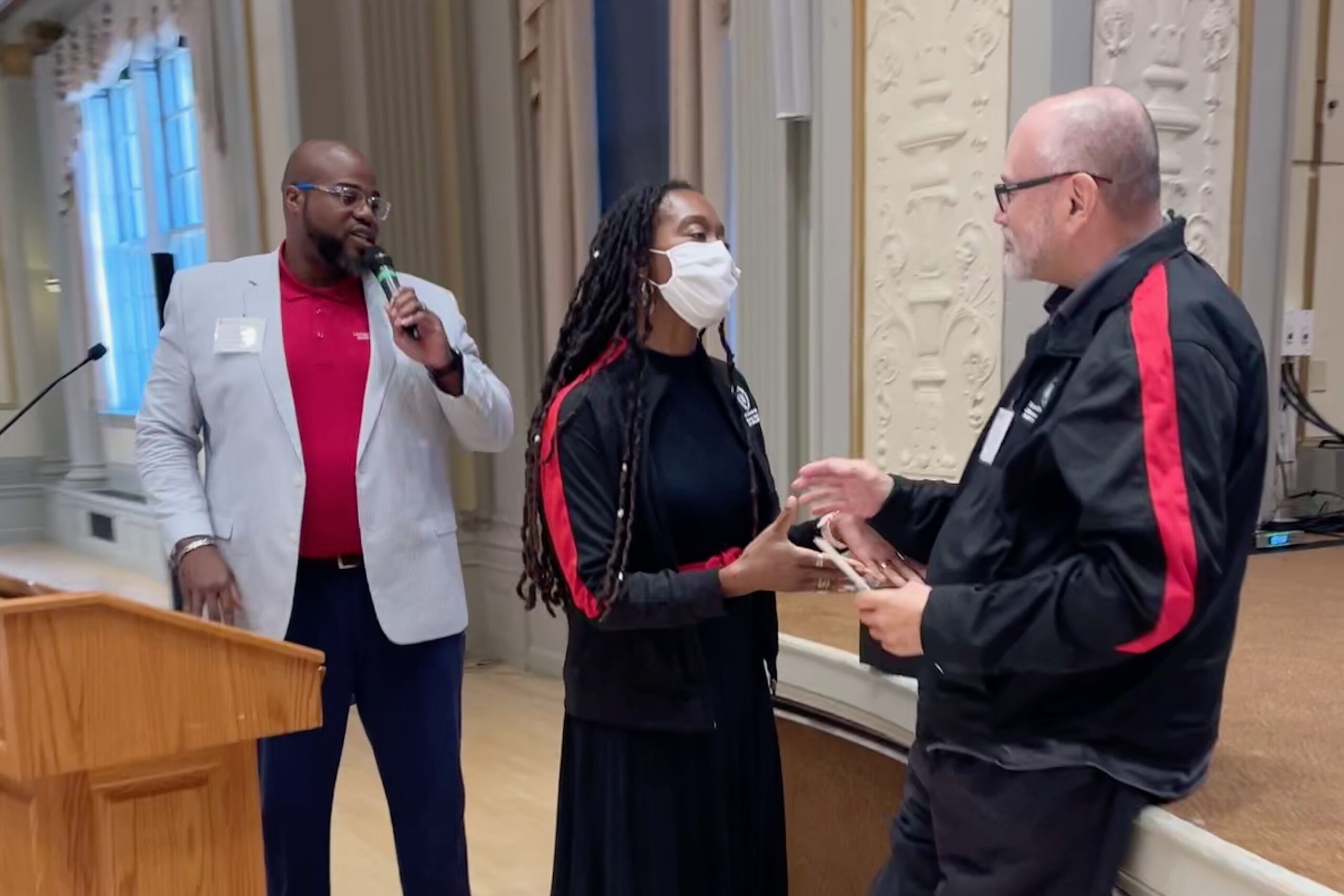 Luis Piñero and Torshieka Maddox shake hands while LaVar Charleston speaks into a microphone.