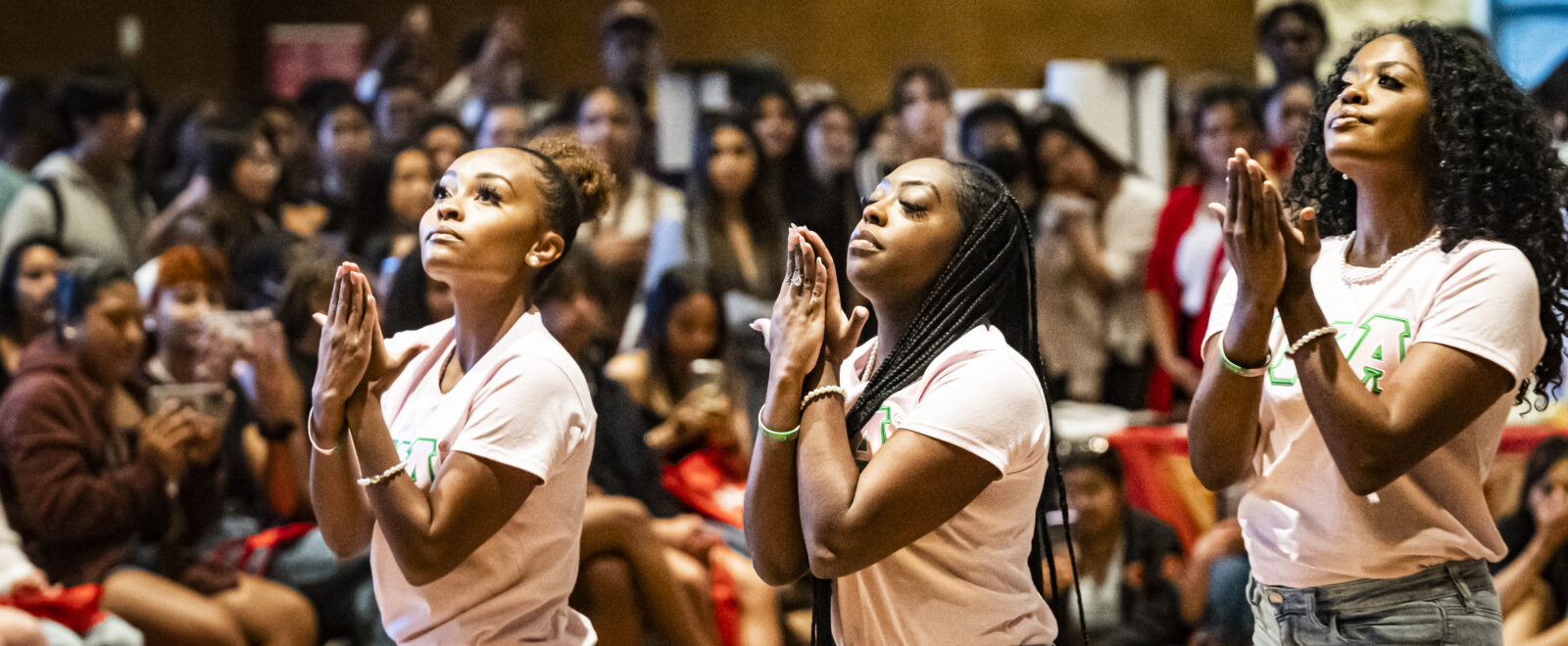 Black women wearing pink Alpha Kappa Alpha Sorority shirts perform a stroll in front of an audience.