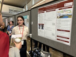 Jehona Zeneli wearing a red lanyard and speaking with someone in front of her research poster.
